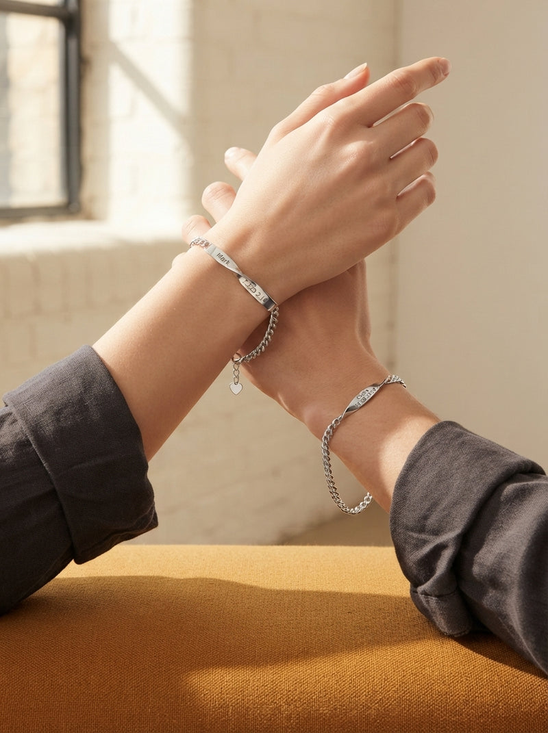 Two hands wearing silver Mobius strip bracelets on wrists, set against a blurred, minimalist background with warm earth tones